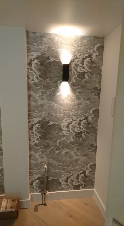 Wand met grijs behang met wolkenmotief en een zwarte wandlamp